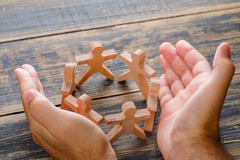 Business success concept on wooden background high angle view. hands protecting wooden figures of people